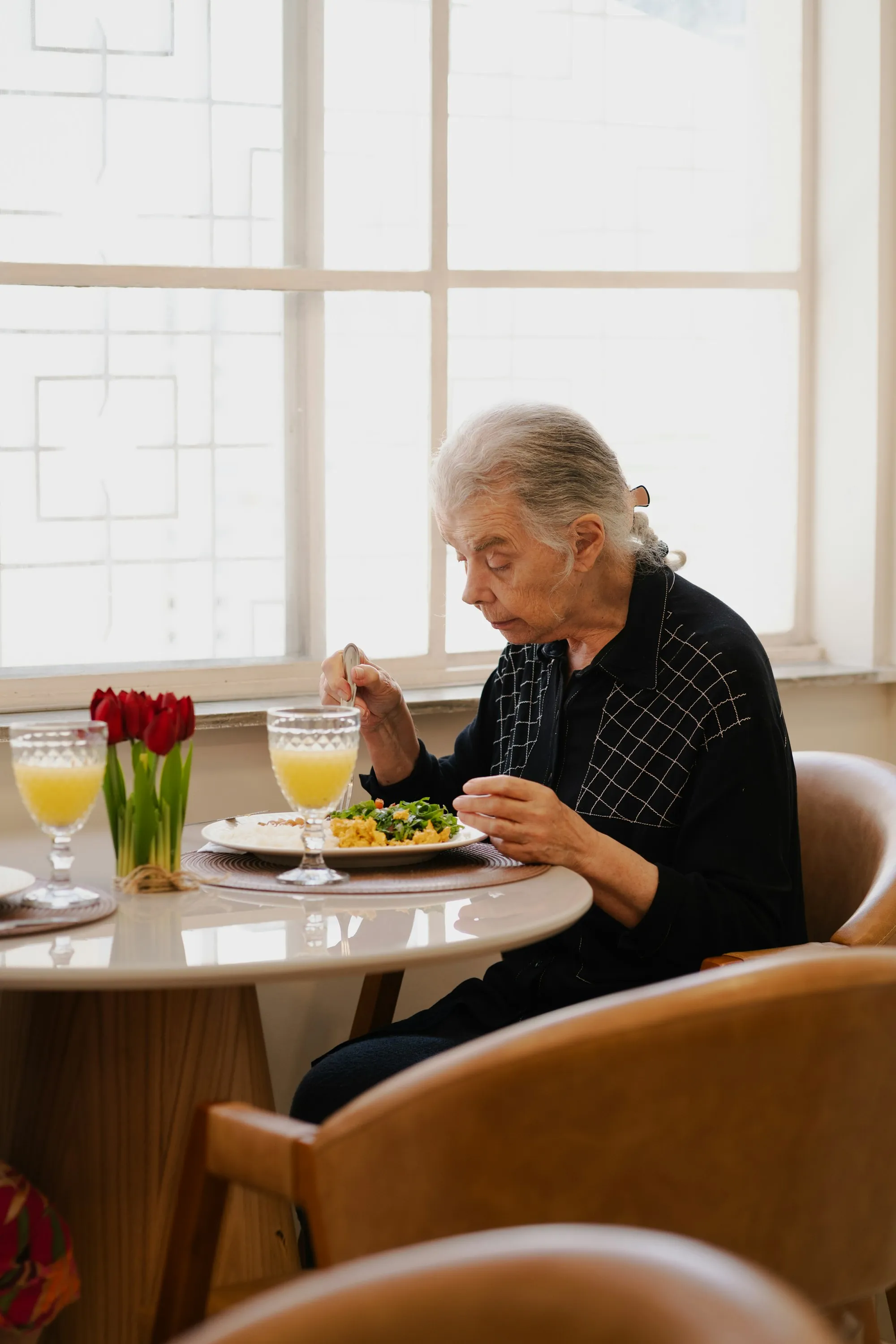 An older woman eating a meal at a table by the window